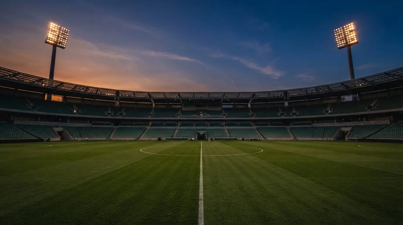 An empty football stadium with floodlight masts at dusk
