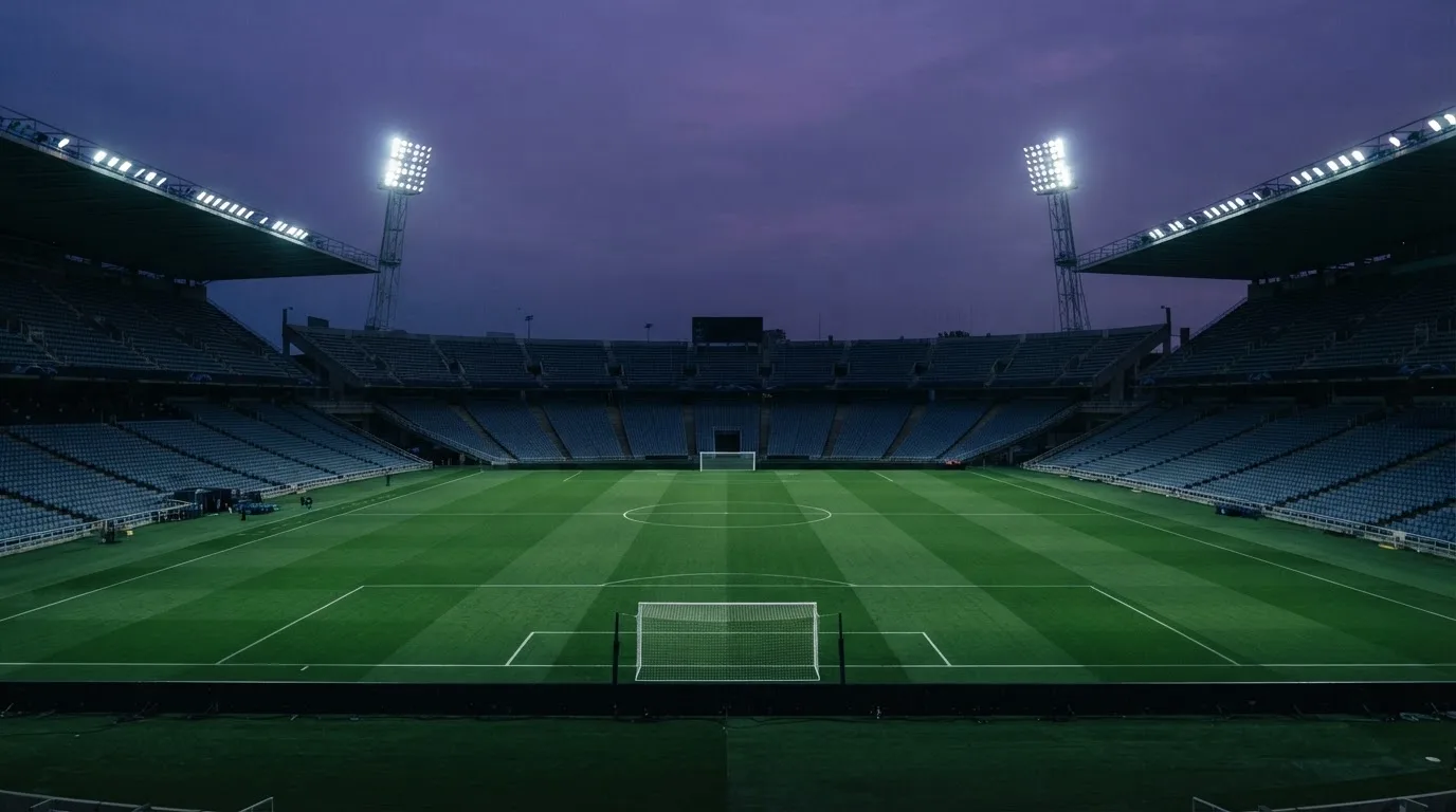 An empty football stadium with floodlight masts at dusk