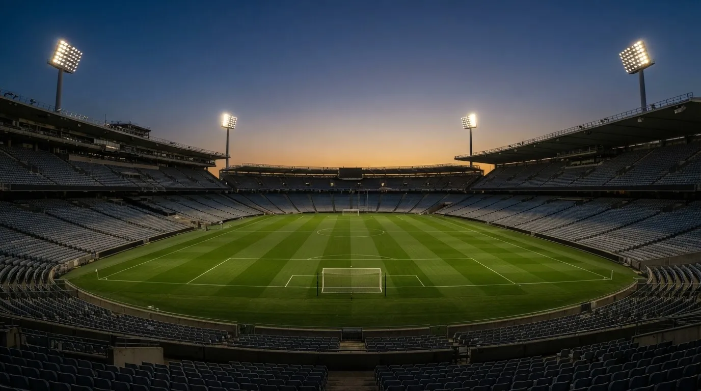 An empty football stadium with floodlight masts at dusk