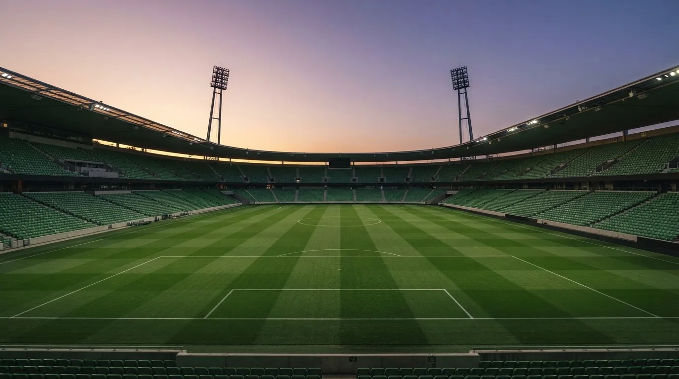 An empty football stadium with floodlight masts at dusk