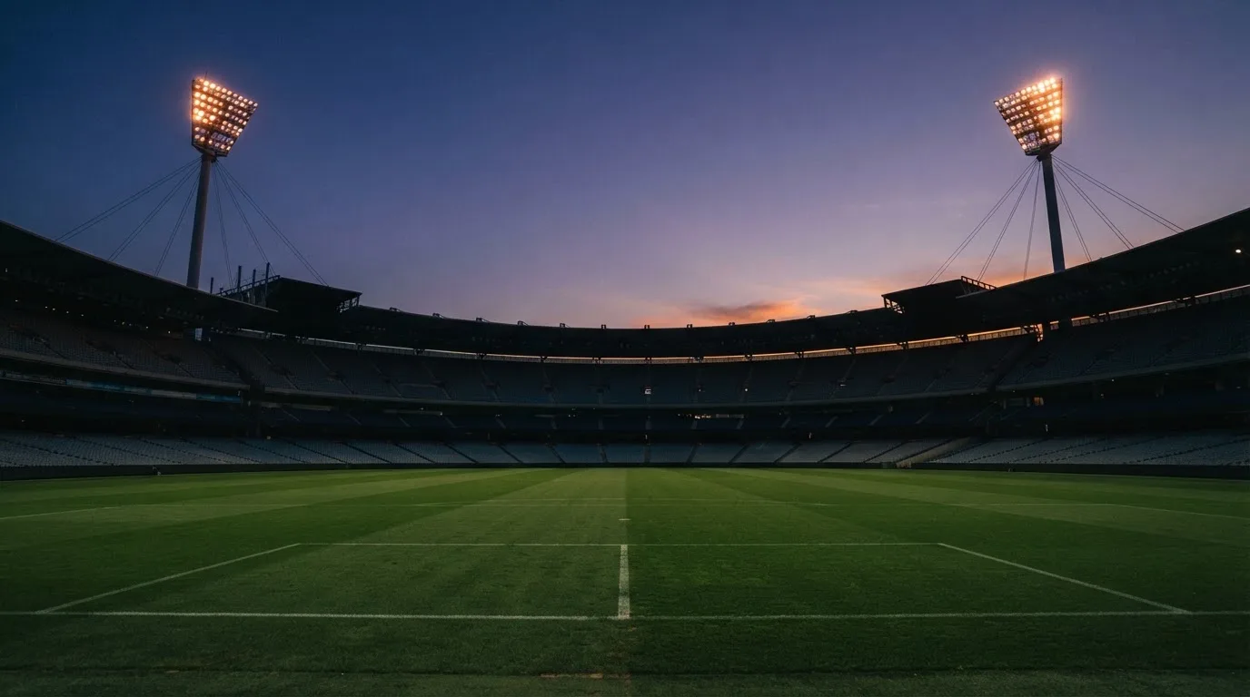 An empty football stadium with floodlight masts at dusk