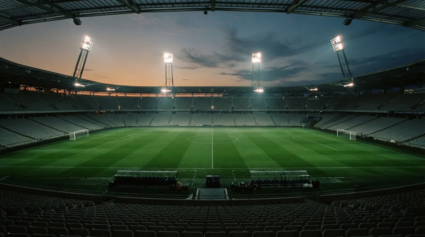 An empty football stadium with floodlight masts at dusk